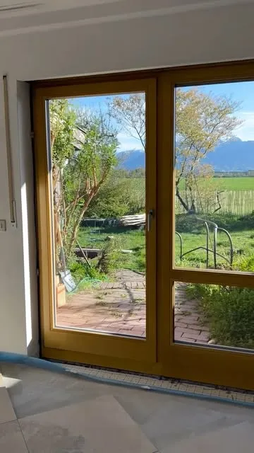 Instagram-Beitrag: zweiflügelige Terrassentür aus Holz mit Blick ins Grüne und auf die Berge