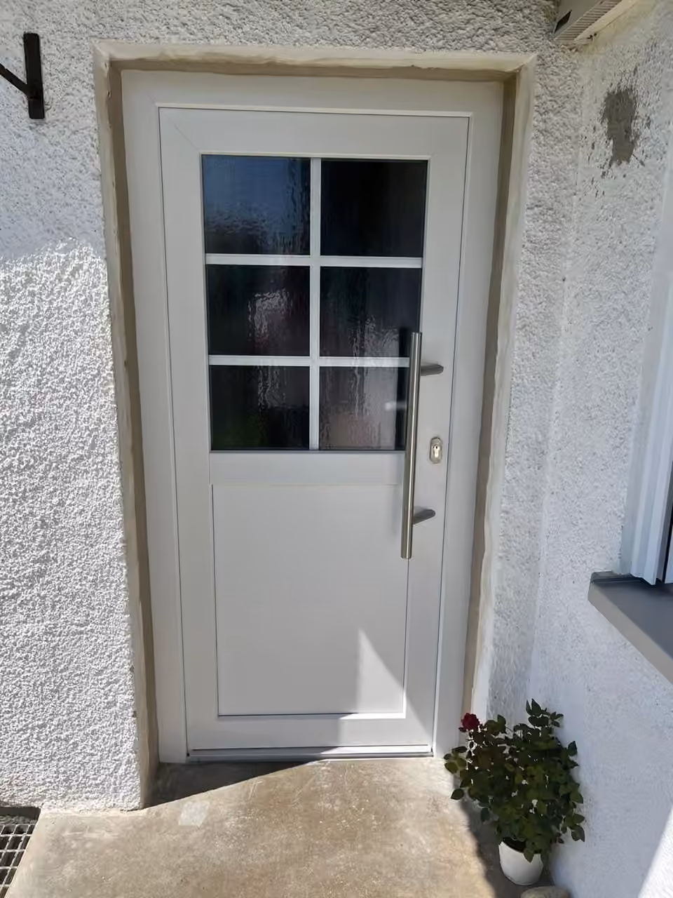 Weiße Haustür mit sechs Sprossenfeldern und Edelstahlgriff an einem verputzten Haus