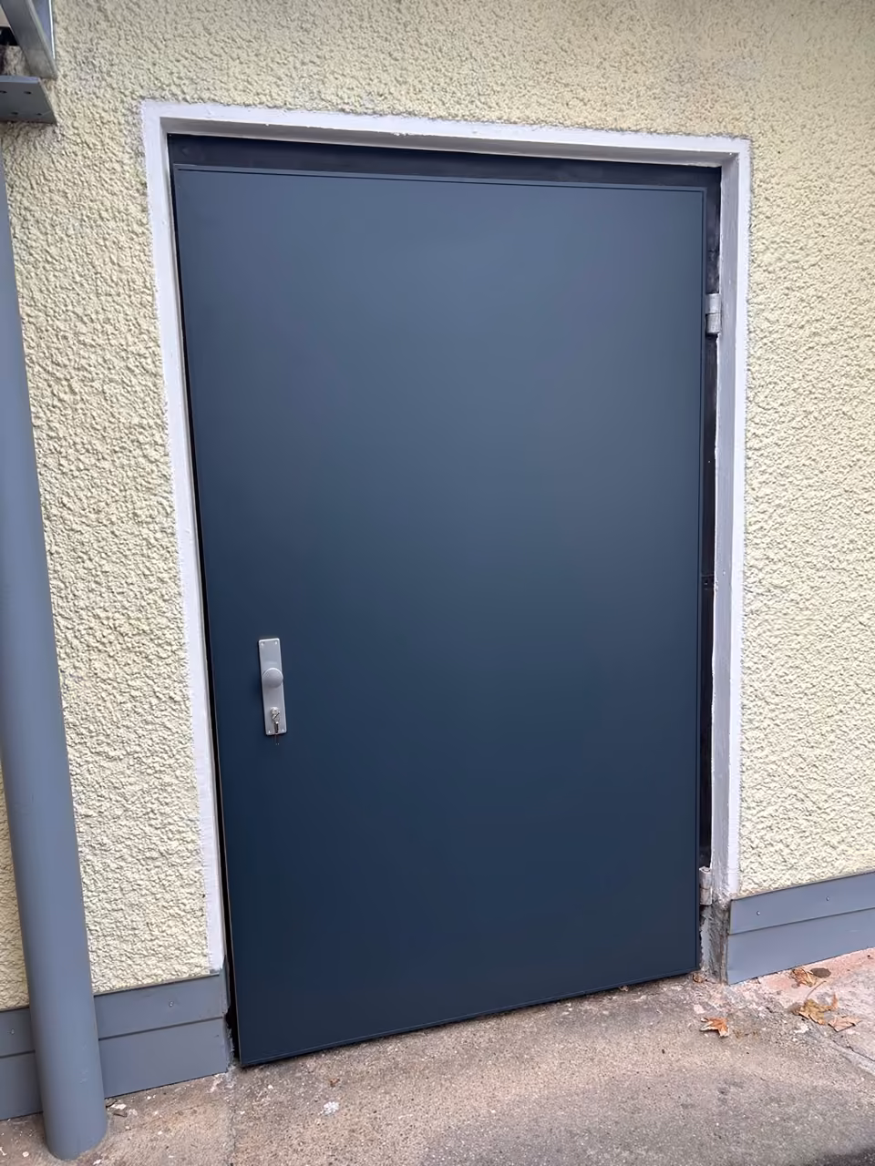 Glatte Nebeneingangstür in Anthrazit mit Edelstahlgriff in einer hellen Putzfassade