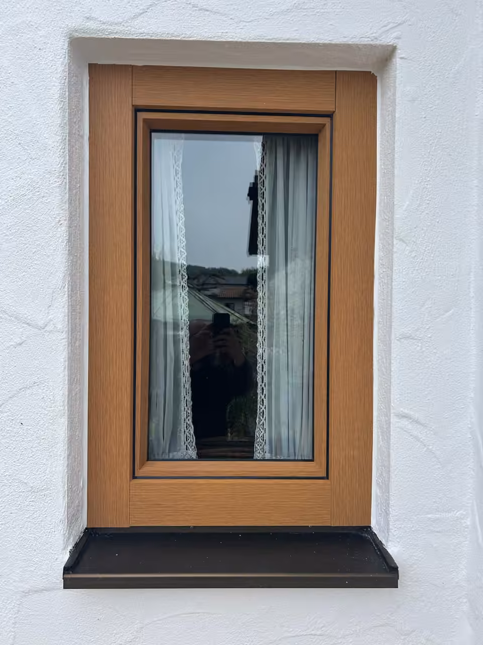 Holzfenster in Eiche mit dunkler Fensterbank in einer weißen Fassade
