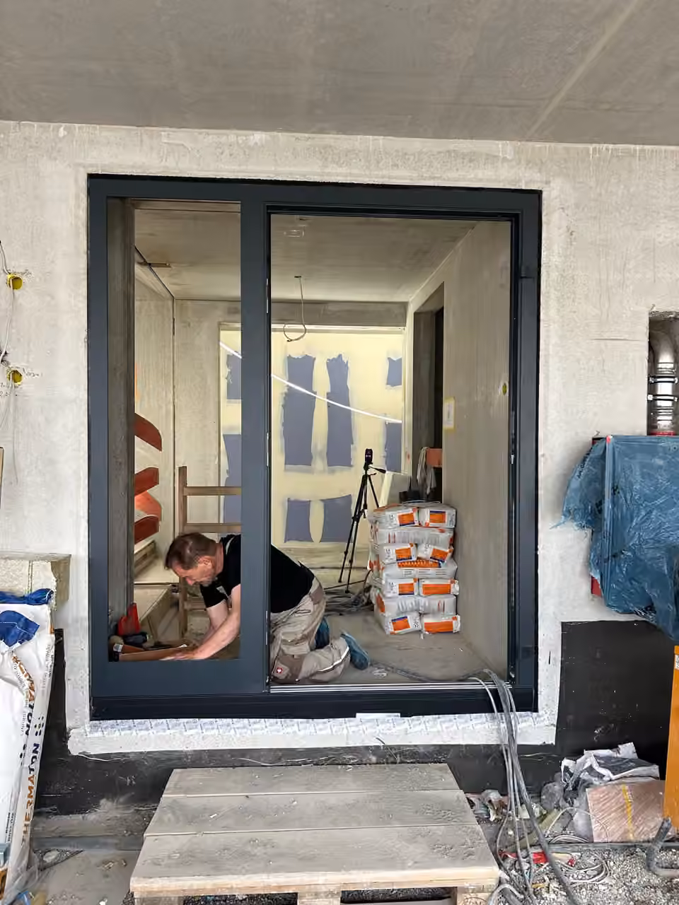 Mitarbeiter kniet beim Einbau einer großen Hebeschiebetür mit dunklem Rahmen