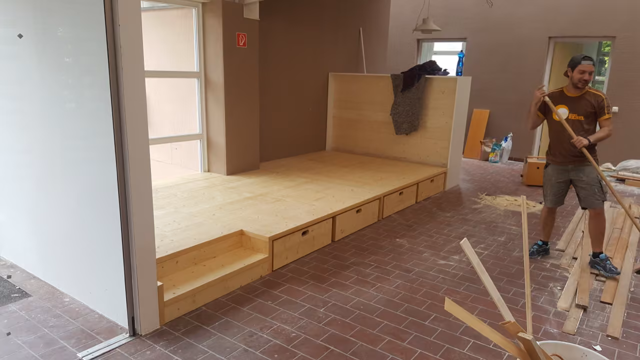 Mitarbeiter baut ein Holzpodest mit Schubladen in einem Gruppenraum ein