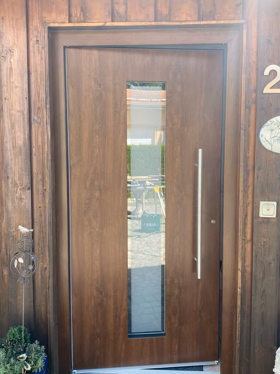 Haustür in dunkler Holzoptik mit senkrechtem Glasstreifen und langem Stangengriff in einer Holzfassade