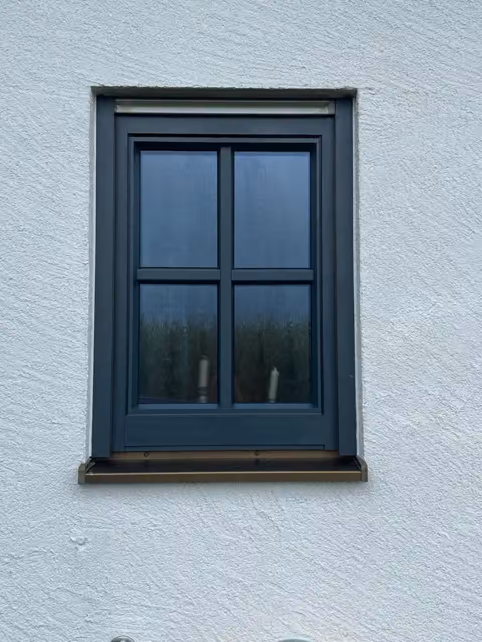 Anthrazitfarbenes Sprossenfenster in einer weiß verputzten Fassade