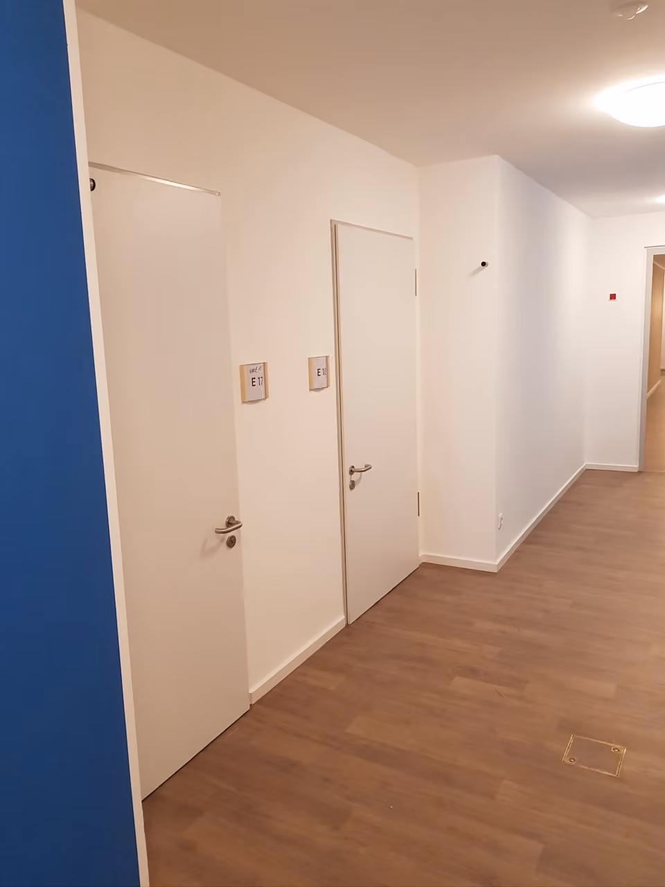 Langer Flur mit weißen Innentüren und Holzboden in einem öffentlichen Gebäude